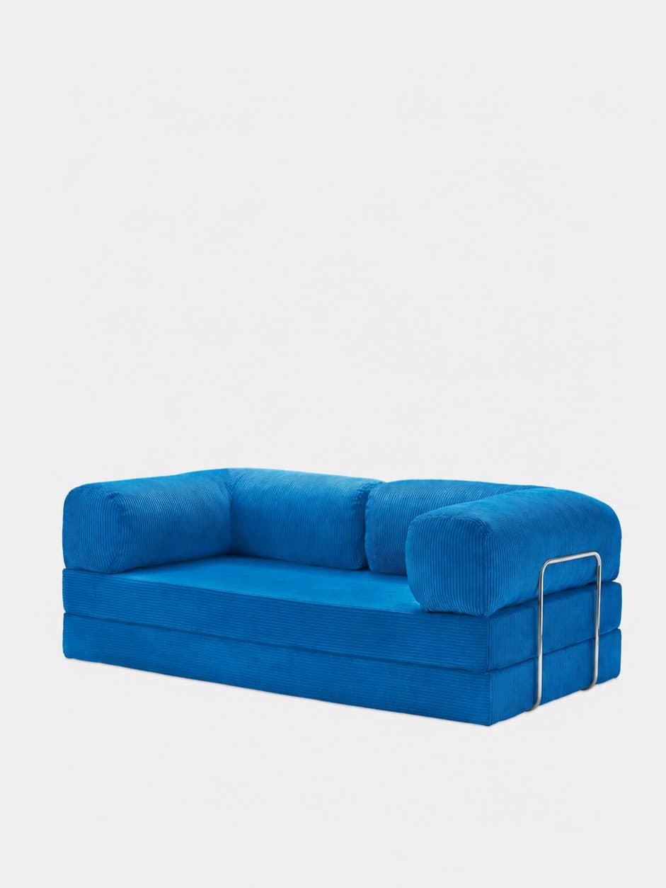 A vibrant blue modular sofa, upholstered in corduroy fabric, featuring a low-profile base composed of foldable segments. It includes cylindrical bolster-style backrests and armrests, with one armrest supported by a polished metal tubular frame. — 3D model