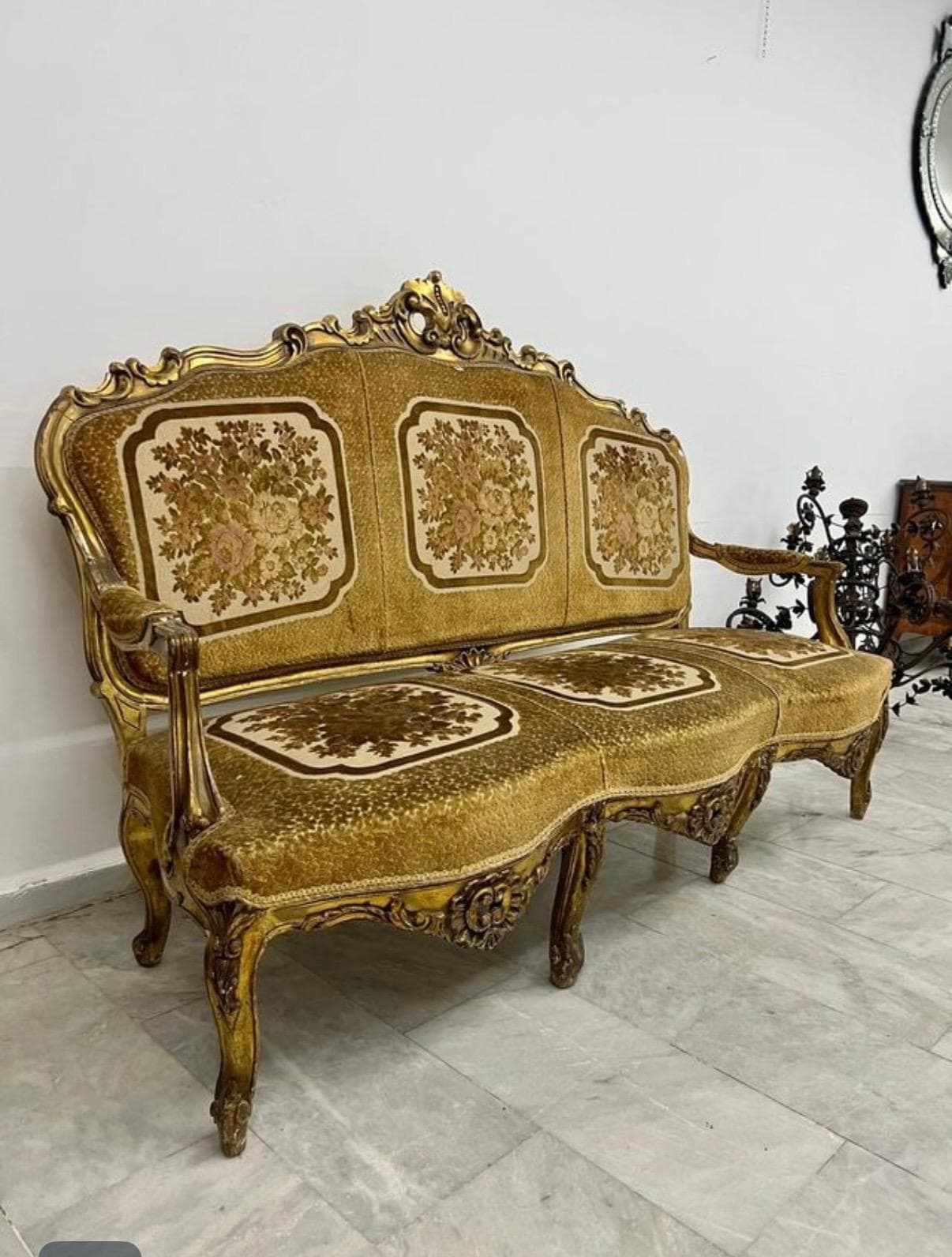 An ornate, gilded three-seater sofa characterized by its elaborate carved wood frame and patterned floral upholstery. The sofa features a curvilinear backrest and armrests, traditional cabriole legs, and individual seat and back cushions adorned with distinct floral motifs. — 3D model