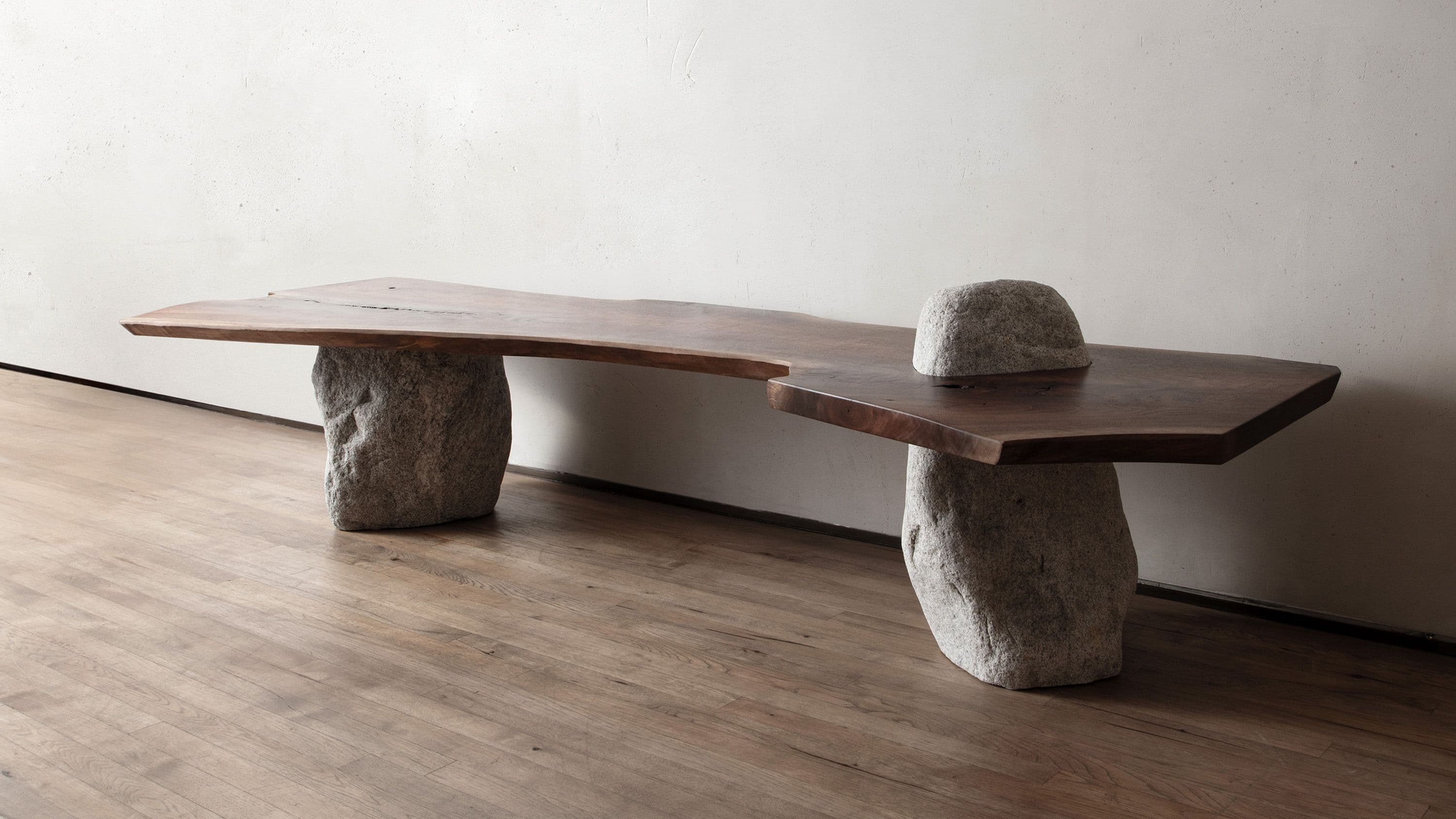 A unique bench featuring a live-edge wooden slab top supported by two irregular, natural stone bases. The wood exhibits a dark brown hue with visible grain and natural imperfections, while the stone bases are light gray and appear rough-hewn, providing a strong textural contrast. The overall design emphasizes natural forms and materials. — 3D model
