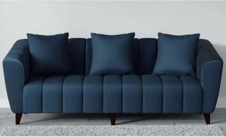 A contemporary blue sofa featuring prominent channel tufting on the seat and backrest, complemented by gently flared arms. It is upholstered in a solid blue fabric and rests on four tapered, dark-stained wooden legs. The sofa includes three matching throw pillows. — 3D model