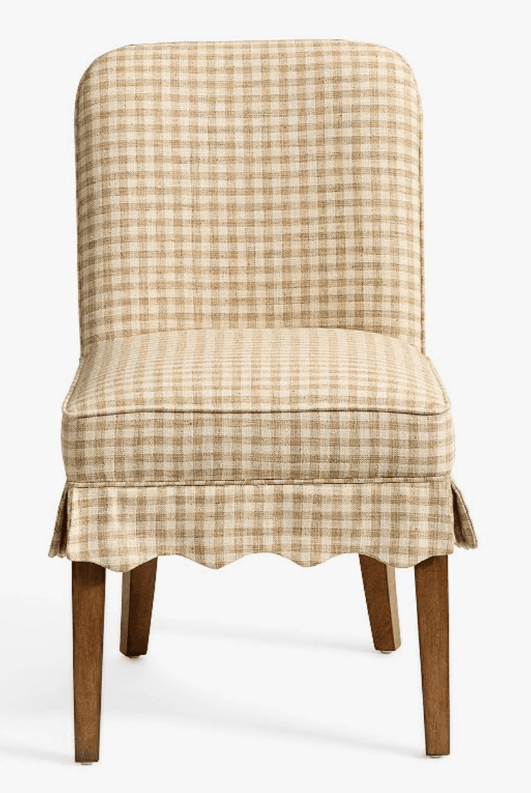 A fully upholstered dining chair featuring a beige and white gingham check pattern. The chair has a tall, slightly curved backrest and a padded seat. A decorative scalloped skirt covers the lower part of the seat frame, partially concealing the upper portion of the four tapered wooden legs. The design suggests a blend of traditional and country-style aesthetics. — 3D model