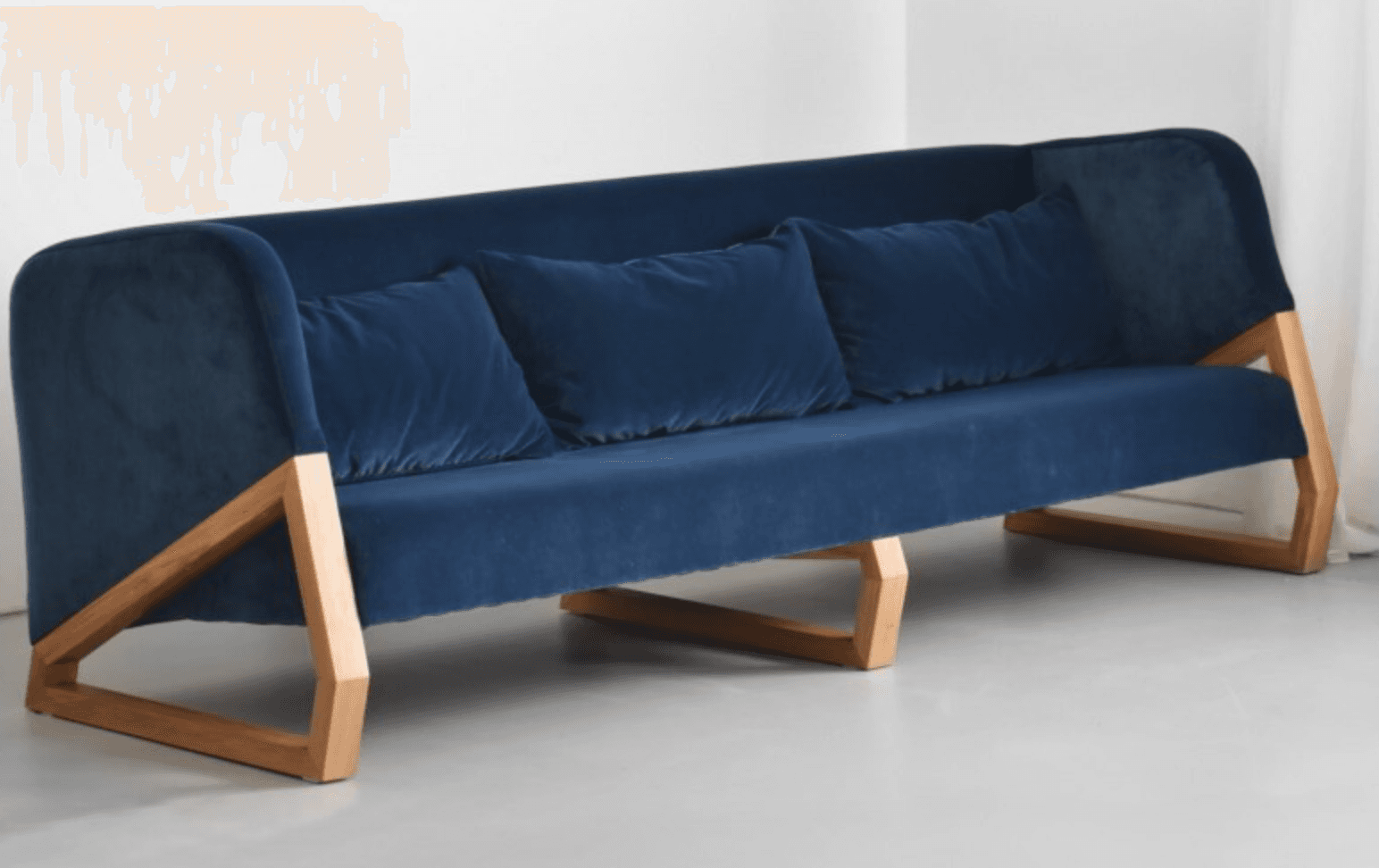 A modern sofa featuring deep blue fabric upholstery and a distinctive exposed light-toned wooden frame. The sofa has a single seat cushion and three loose back cushions, with a gently sloped back and integrated armrests that flow into the overall form. The unique wooden frame forms an angular support structure beneath the upholstered body. — 3D model