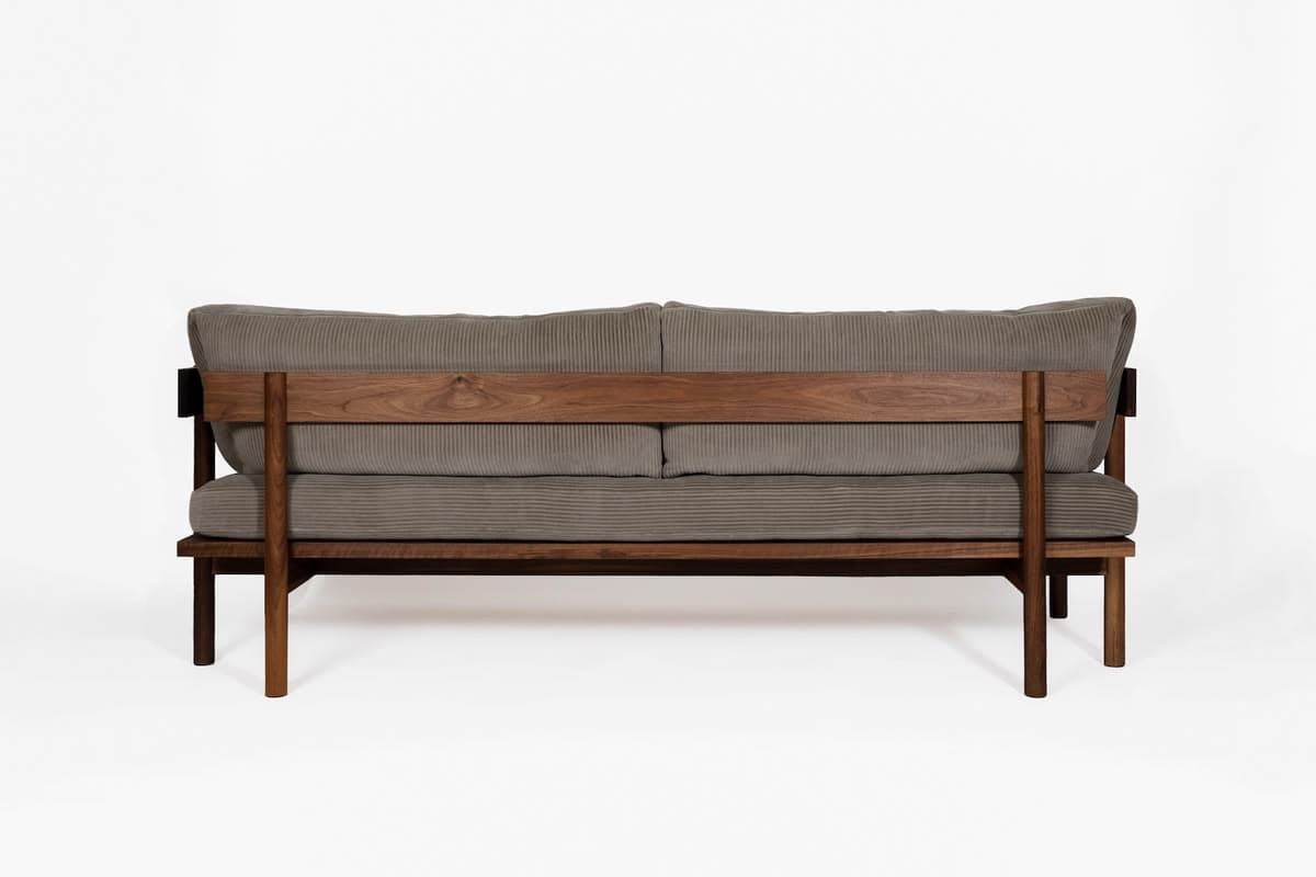 A contemporary loveseat featuring a robust dark wood frame and plush grey corduroy upholstery. The design emphasizes clean lines and a minimalist aesthetic. The backrest consists of two large, soft cushions supported by a wide horizontal wooden slat and vertical posts, which are part of the exposed wooden frame. The seat also has two substantial cushions, matching the back. The frame includes four sturdy, straight legs, with the rear legs appearing slightly splayed. The overall construction suggests durability and modern design principles, with the texture of the ribbed fabric adding visual interest. — 3D model