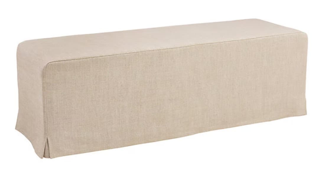 A rectangular, upholstered bench featuring a full-length, light-colored fabric slipcover that extends to the floor, creating a skirted base with small kick pleats at the corners. — 3D model