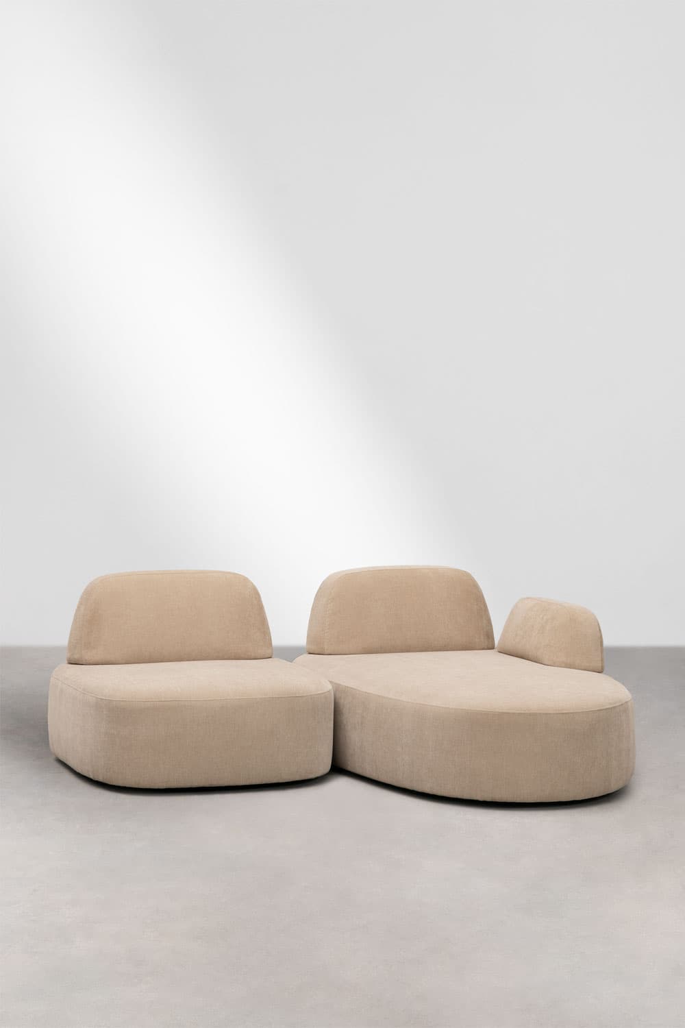 A modular, low-profile sofa with rounded edges and plush upholstery. The sofa consists of two distinct sections: a left section that appears to be an armchair or a single seating unit, and a right section that forms a chaise lounge. Both sections have integrated, curved backrests and are upholstered in a textured, light beige fabric. The overall design is modern and organic. — 3D model