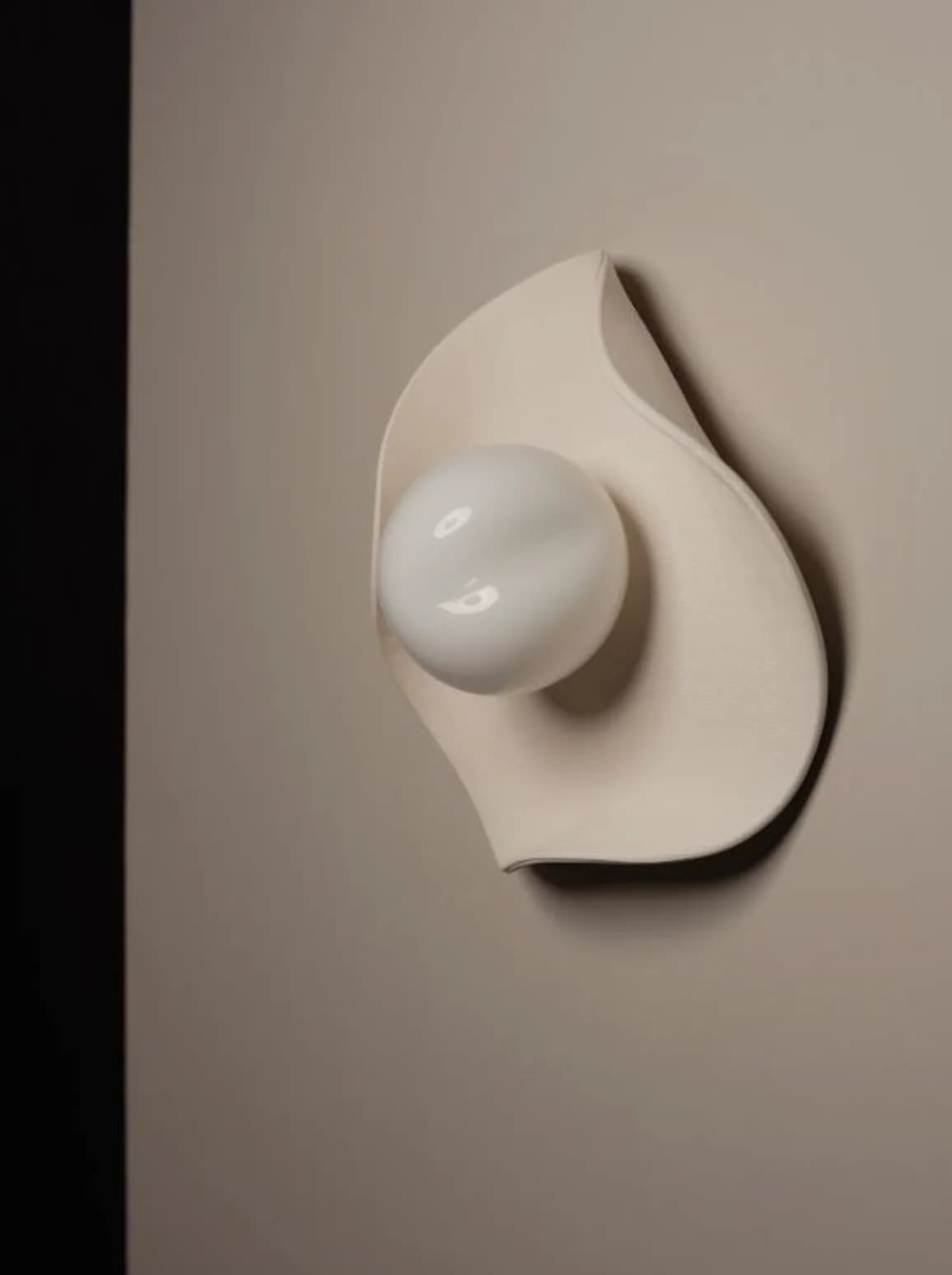 A modern sculptural wall sconce featuring an organic, leaf-like cream-colored backplate made of ceramic or plaster, paired with a spherical frosted glass diffuser. The design is minimalist and fluid, providing soft, diffused illumination. — 3D model