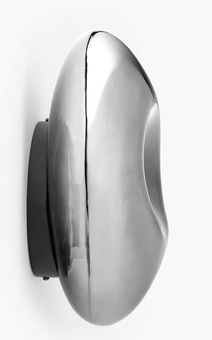 A modern wall-mounted light fixture featuring a fluid, organic, and irregularly shaped front in a highly polished chrome or metallic finish. It is mounted on a flat, dark backplate, contrasting with the reflective, undulating surface of the main light element. The design is sculptural and abstract, intended to provide ambient light while serving as a decorative art piece. — 3D model