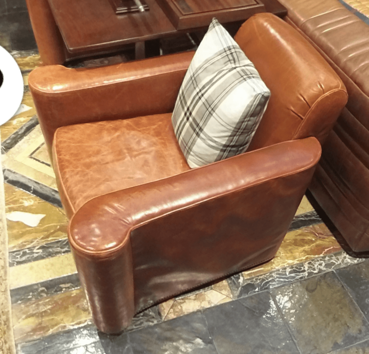 A brown leather armchair with a plaid cushion placed on the seat. The armchair has rolled arms and a slightly distressed leather finish. The backrest is visible, as is part of the seat and the front of the rolled arms. — 3D model