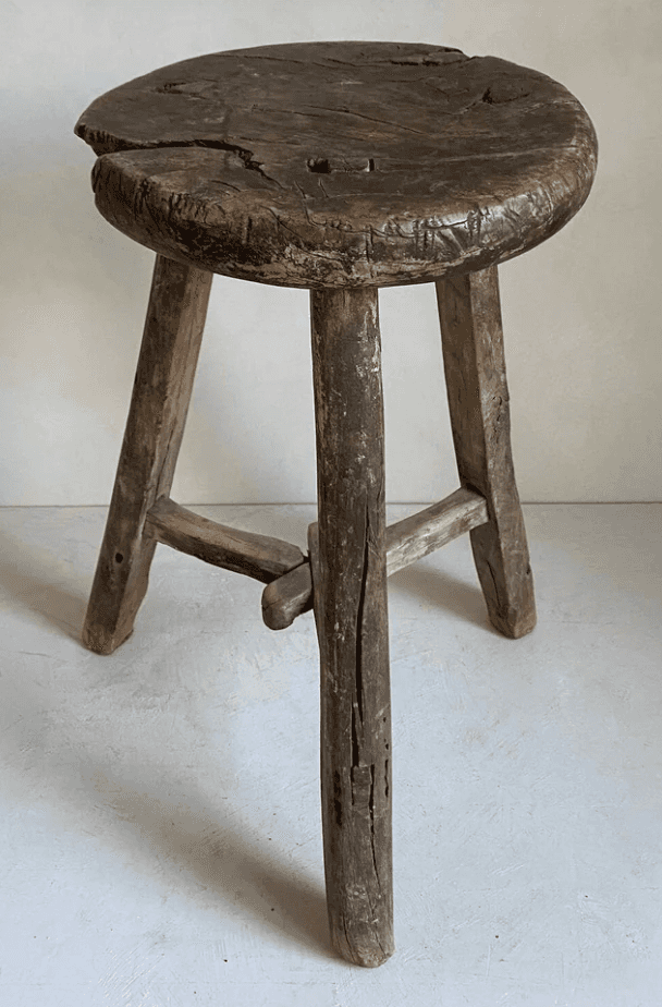 A rustic, round-top stool with three legs. The stool is constructed from weathered wood and shows si… — 3D model