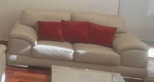 A modern two-seater sofa upholstered in light beige material, featuring three red throw pillows. It… — 3D model