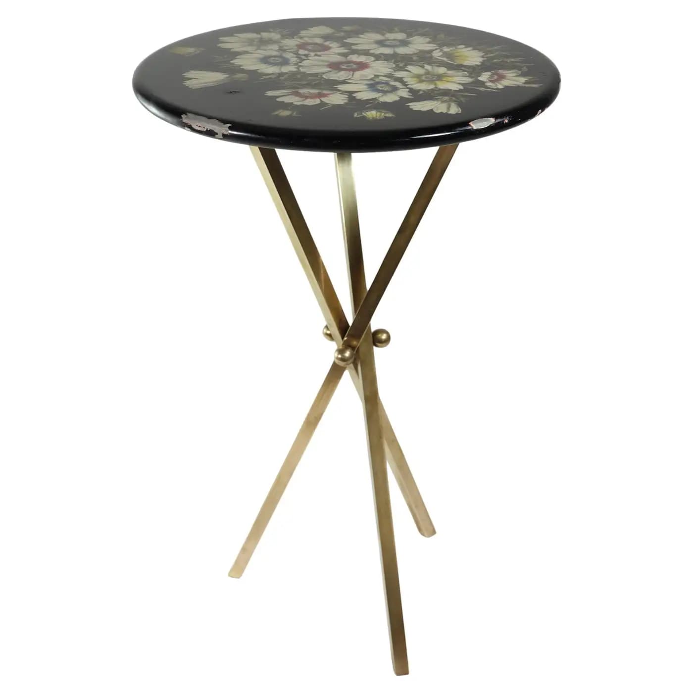 A small, round black table featuring a multi-color floral motif painted on its lacquered top, supported by a gold-toned metal X-frame base. The tabletop shows visible wear and chipping along its edges, revealing lighter material beneath the black finish. The base consists of four slender, straight legs, joined at the center in an X-shape. — 3D model