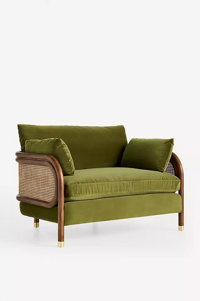 A contemporary lounge chair upholstered in olive green velvet, featuring a dark wood frame with curved armrests and woven cane side panels. It includes plush seat, back, and accent cushions, supported by dark wooden legs capped with brass accents. — 3D model