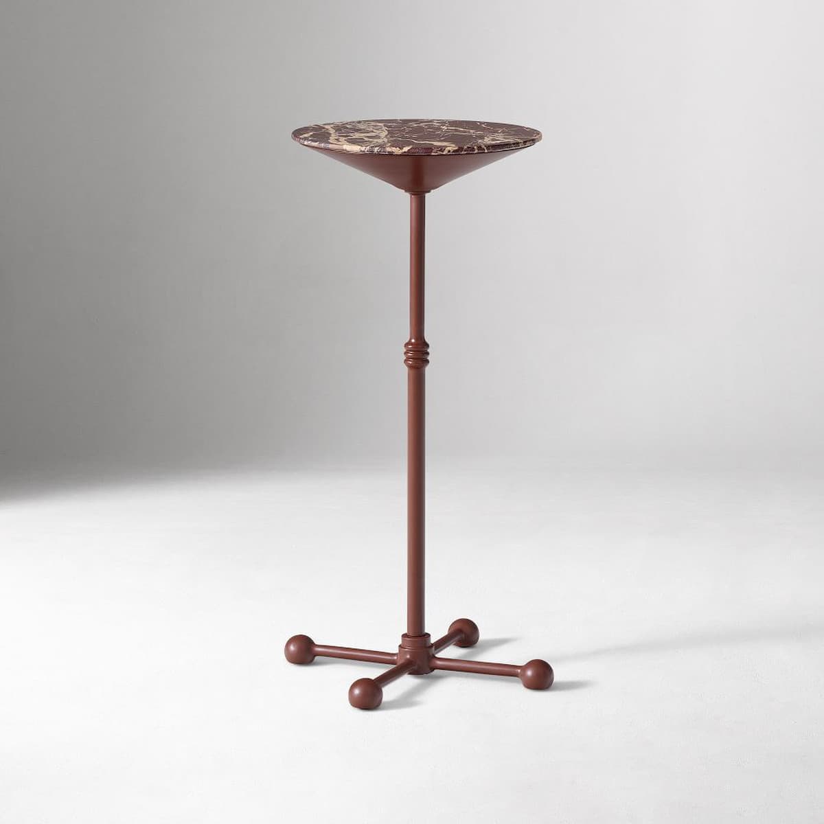A tall, slender pedestal accent table featuring a round, mottled brown marble top. The table is supported by a single, reddish-brown column with a turned detail in the middle, resting on a four-pronged base with spherical feet. — 3D model