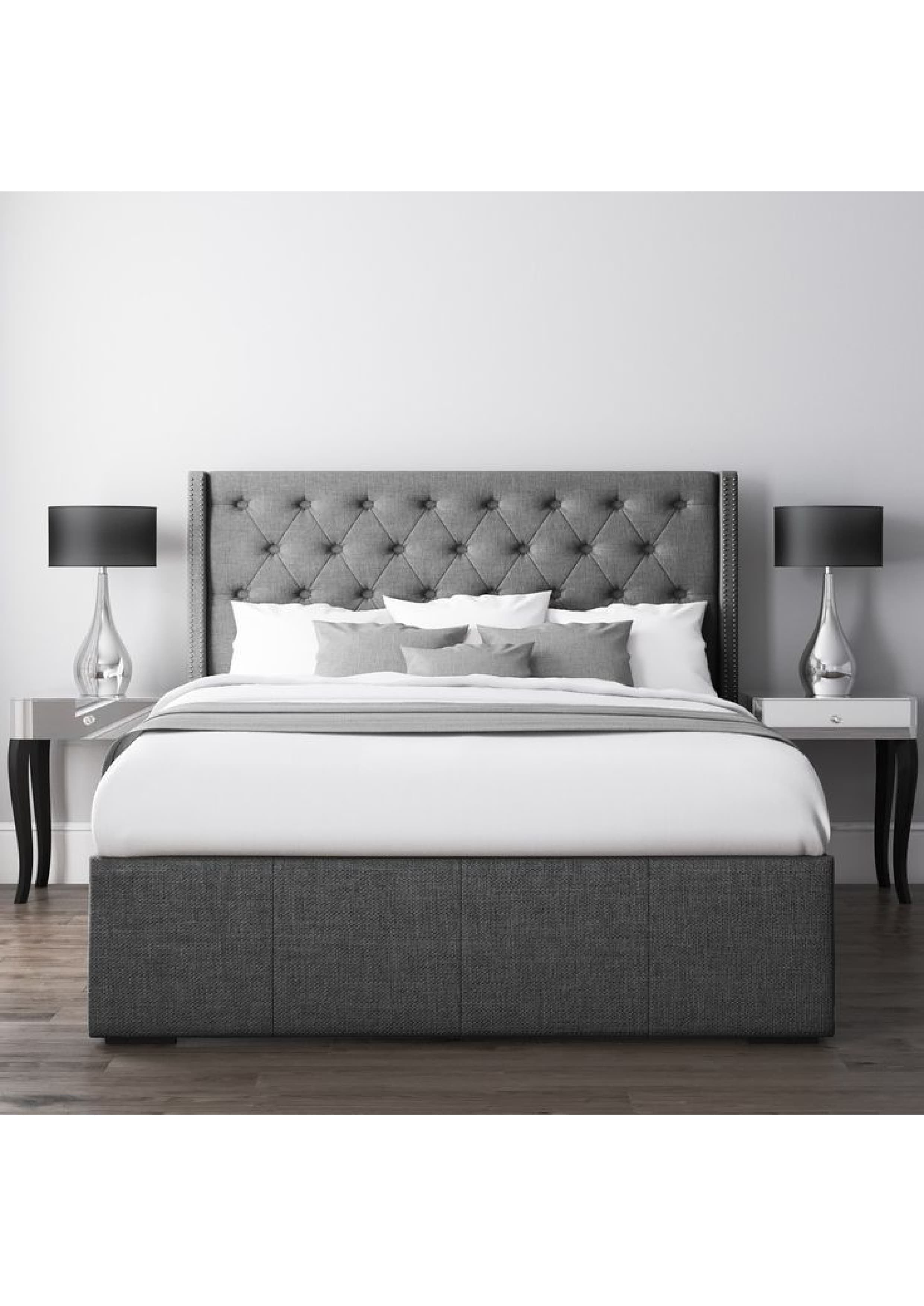 A contemporary upholstered bed featuring a gray fabric finish, a tall button-tufted headboard with a wingback design and silver nailhead trim. The bed includes an integrated platform base with visible storage drawers. The bed is dressed with white bedding, gray pillows, and a gray throw. — 3D model