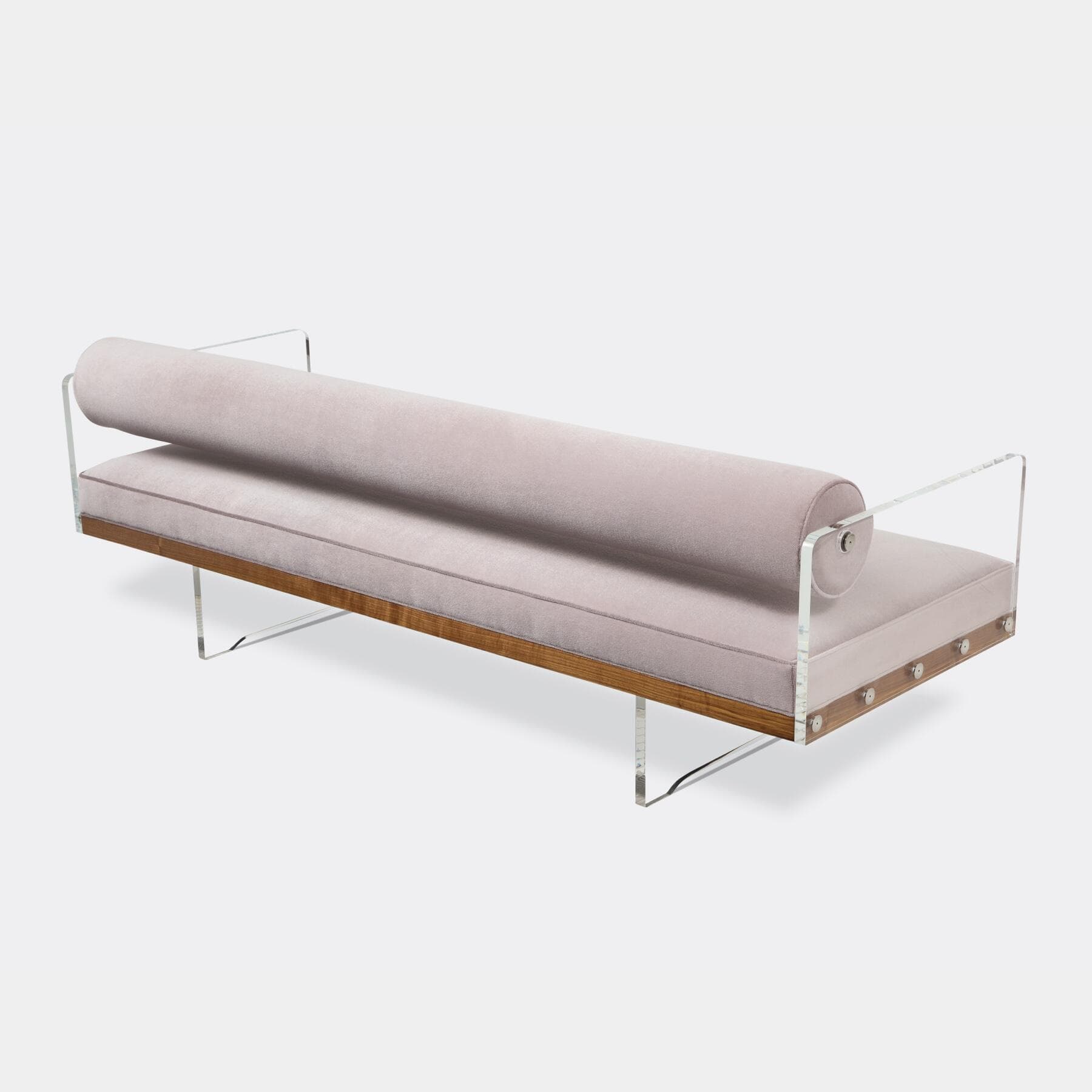 A sleek, modern daybed featuring a rectangular seat cushion and a cylindrical bolster backrest, both upholstered in a soft, light pink velvet. The seating elements rest on a visible walnut wood base, which is supported by transparent acrylic (Lucite) side panels that also hold the bolster cushion in place. Exposed circular fasteners with a polished finish are visible along the side of the wooden base. — 3D model