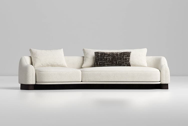 A contemporary three-seater sofa upholstered in a cream or off-white boucle fabric, featuring a low-profile design with subtly rounded arms. The sofa rests on a dark, recessed plinth base, creating a floating effect. It includes two large seat cushions and two matching back cushions, along with one contrasting rectangular accent pillow. — 3D model