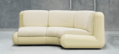 A cream-colored sectional sofa with a curved design. The sofa features multiple seating cushions and a rounded armrest that extends along the sides and front. The base and exterior frame appear to be made of a smooth, possibly lacquered or plastic material, contrasting with the textured fabric of the cushions. — 3D model