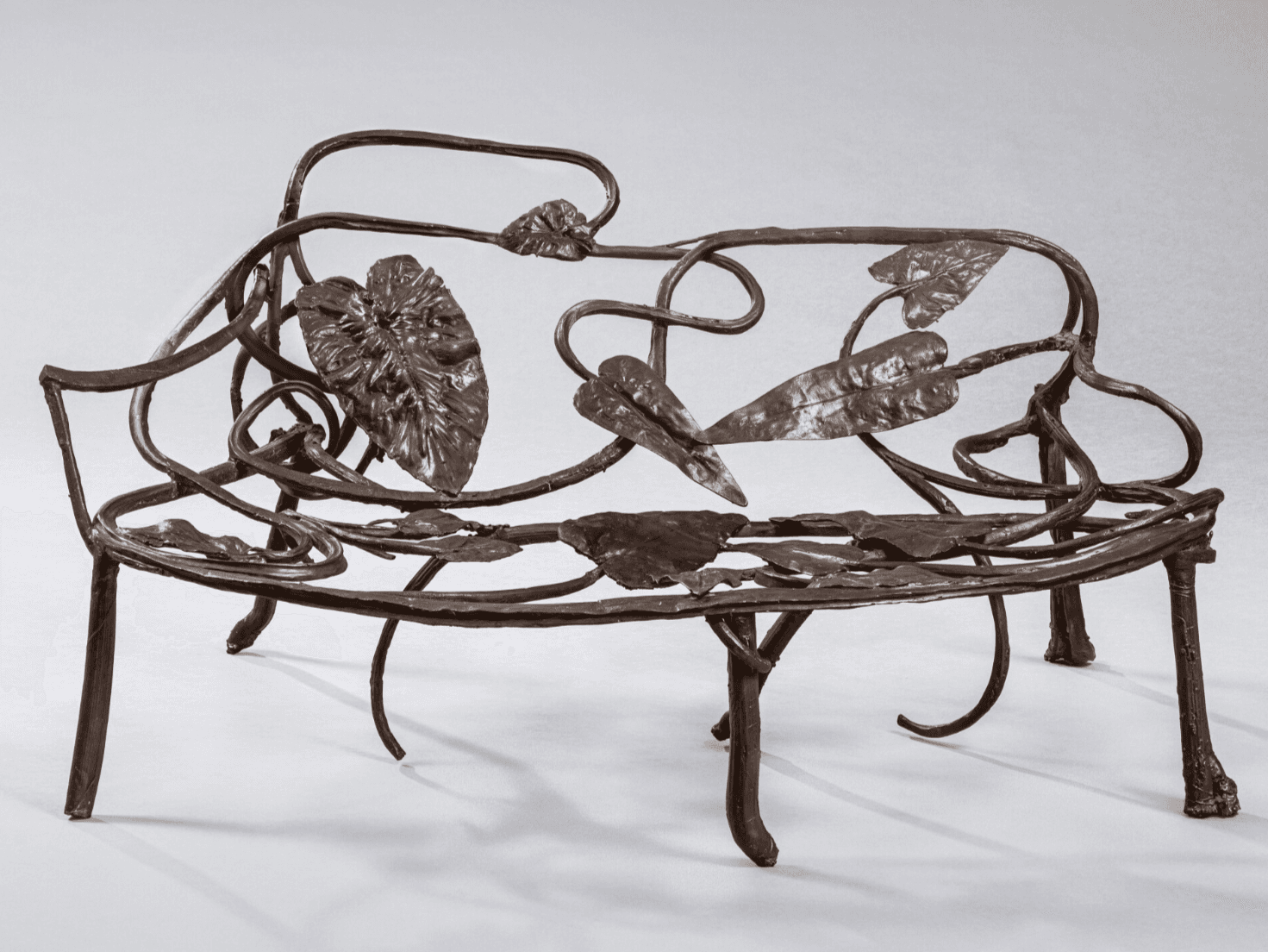 An ornate metal bench featuring a design inspired by nature, with curved metalwork resembling vines and detailed leaf motifs adorning the backrest and seat. The structure has a rustic and artistic appearance. — 3D model