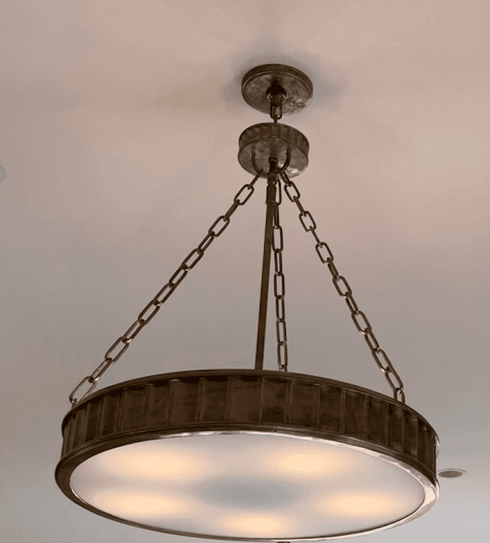 A rustic-style chandelier featuring a drum-shaped shade with a ribbed metal band around its circumference. The fixture is suspended from the ceiling by a series of metal chains, attached to a decorative ceiling canopy. The shade appears to be made of frosted glass, diffusing light from internal bulbs. — 3D model