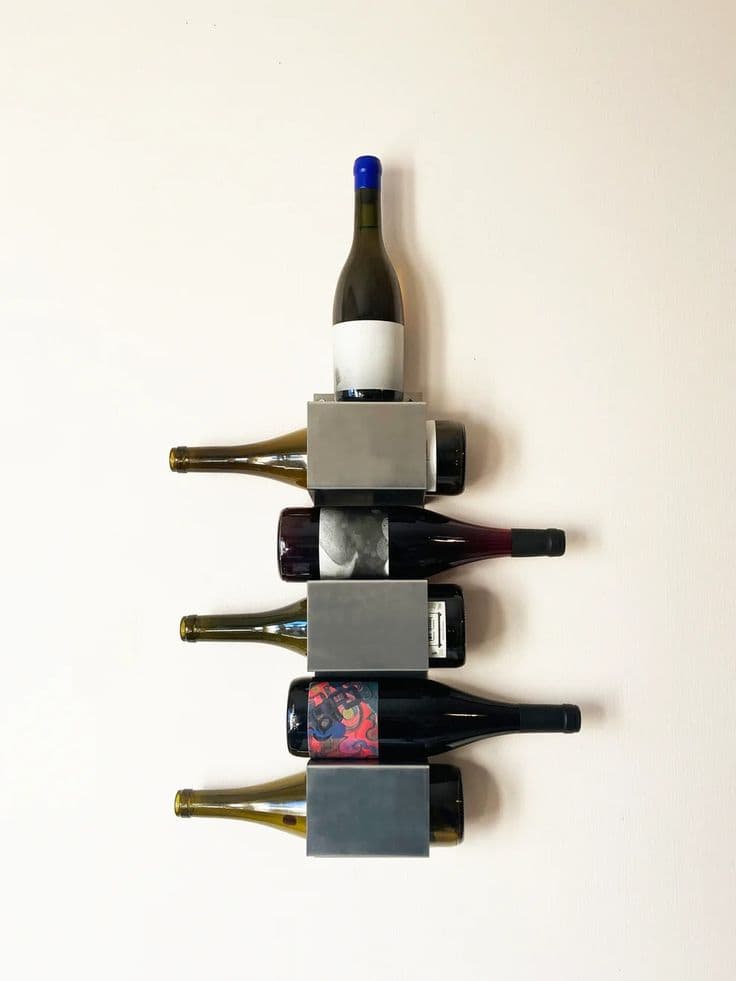 A minimalist wall-mounted wine rack made of brushed metal, designed to store multiple wine bottles horizontally and feature one bottle vertically on top. The rack consists of stacked rectangular modules, each capable of holding one bottle. — 3D model