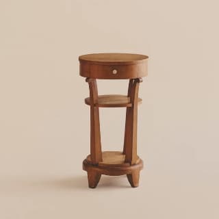 A small, round, wooden side table with a single drawer and a lower shelf. The table features a circular top, an apron with a drawer front and a small knob, and four curved legs that extend from a circular base. A second, smaller circular shelf is positioned midway up the legs. The overall construction suggests a handcrafted piece. — 3D model