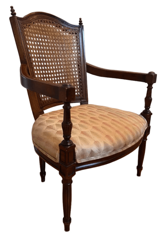 A traditional armchair featuring dark-stained carved wood construction and an upholstered seat. The chair has a solid wood back panel framed by a curved top rail with decorative finials. The front legs and arm supports are turned and fluted, showcasing intricate detailing. The seat cushion is upholstered in a multi-colored geometric patterned fabric, predominantly beige with accents of pink and green. — 3D model