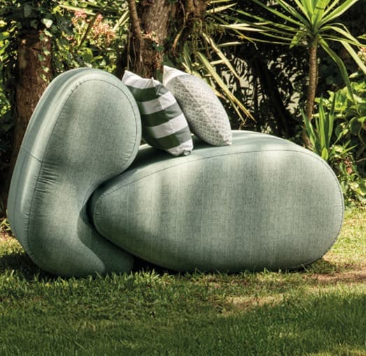An upholstered lounge chair with an organic, sculptural form, featuring a light green textured fabric and two decorative throw pillows. — 3D model