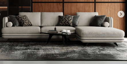 An L-shaped sectional sofa featuring a right-hand facing chaise lounge, upholstered in a light, neutral-toned fabric. The design is contemporary, characterized by clean lines, rounded edges on the arms and back, and distinctive dark contrast piping tracing the seams along the base, arms, and back cushions. The sofa sits on short, dark, tapered legs. It is adorned with several patterned throw pillows in contrasting dark grey and brown tones, adding visual interest to the minimalist base. — 3D model