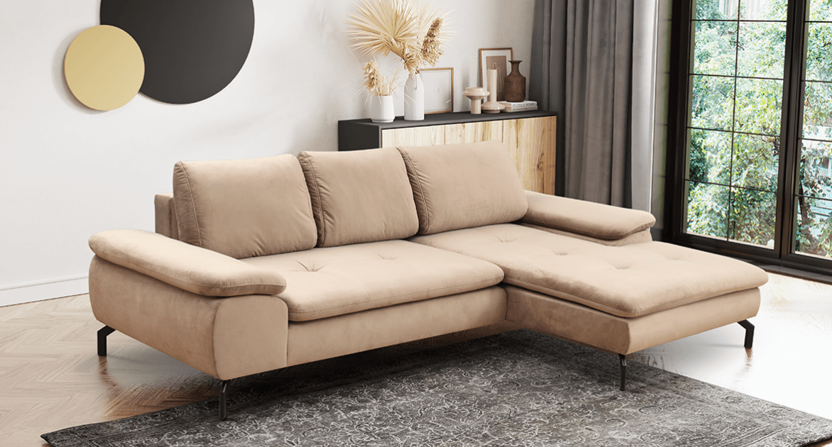 An L-shaped sectional sofa with a right-facing chaise lounge, upholstered in a light beige fabric. It features three loose back cushions and two fixed seat cushions on the main sofa, with a single, longer fixed cushion forming the chaise. The armrests are subtly rolled and padded. The sofa is supported by slender, angled black metal legs, providing a contemporary aesthetic. Subtle button tufting is visible on the chaise section's seating surface. — 3D model