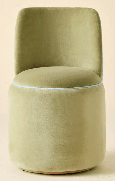 A fully upholstered accent chair featuring a low, curved backrest and a circular seat, both resting on a seamless cylindrical base. The entire piece is covered in a plush pistachio green velvet, accented by thin light blue piping around the edge of the seat and along the contours of the backrest. The chair has no visible legs, contributing to its monolithic and modern appearance. — 3D model