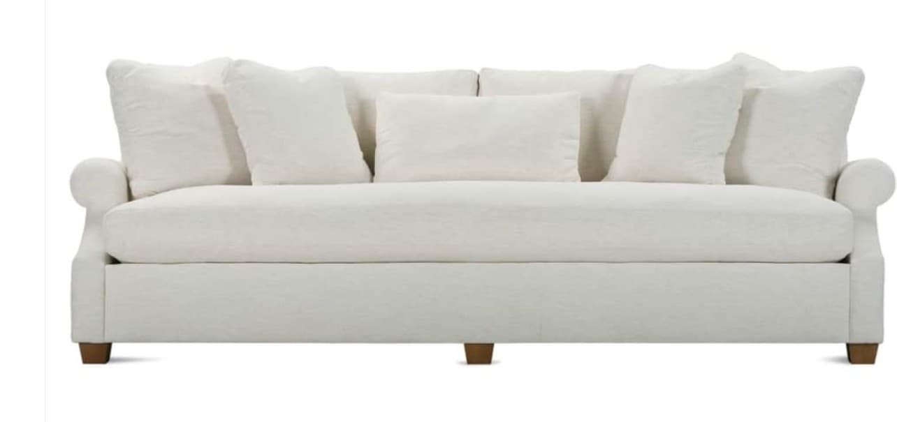 A plush, overstuffed sofa with a clean, tailored base and rolled arms. It features multiple loose back cushions and a solid seat cushion. The sofa is upholstered in a light-colored fabric and supported by short, dark wooden legs. — 3D model