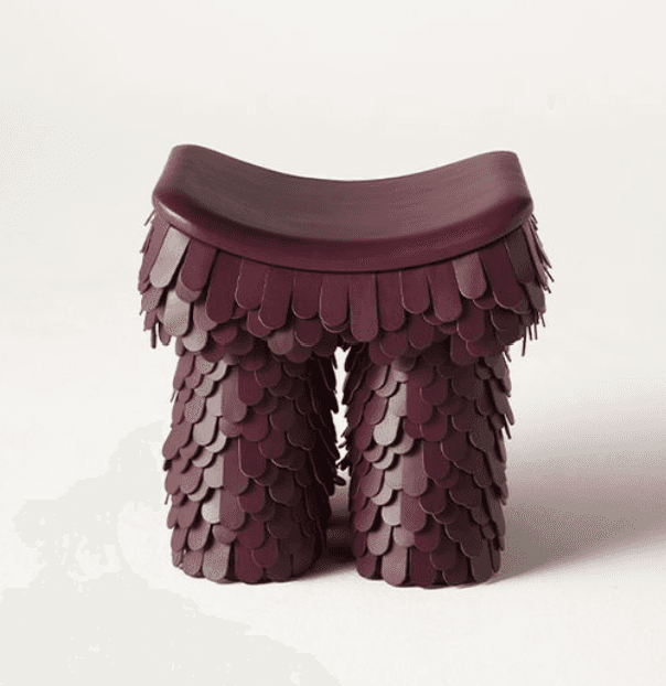 A burgundy, saddle-seat stool featuring a unique, scale-like textured base. The seat is smoothly cur… — 3D model