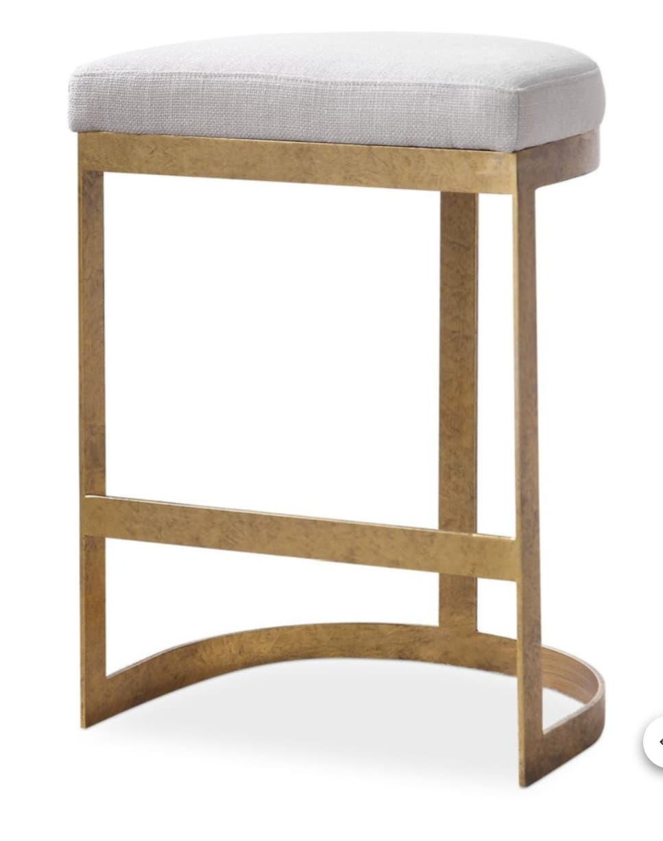 A tall, backless stool featuring a cushioned, upholstered rectangular seat in a light fabric, supported by a distinctive C-shaped distressed gold-finished metal frame that includes a horizontal footrest bar. — 3D model