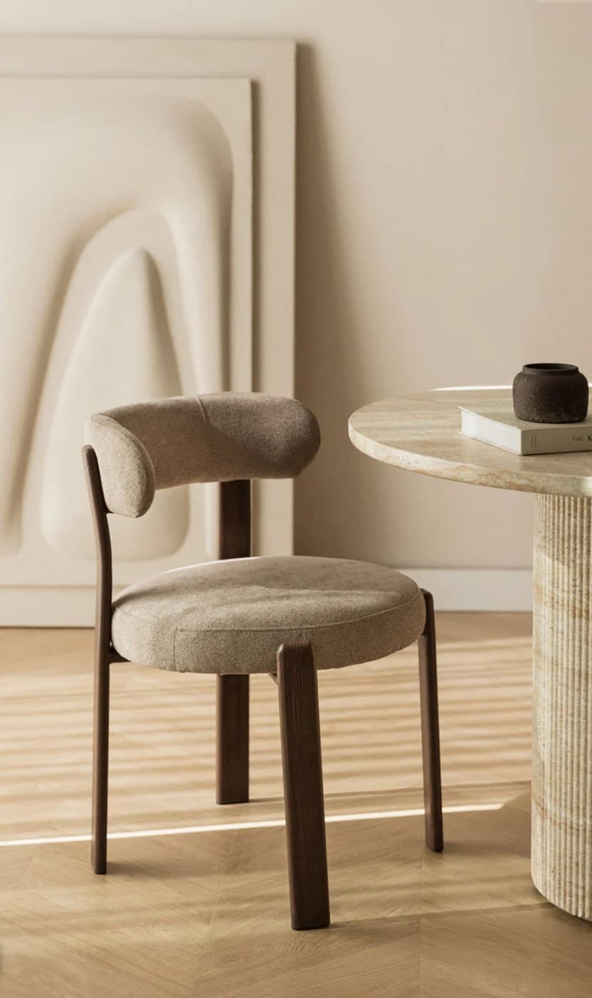 A modern accent chair with a rounded backrest and a circular seat. The frame appears to be constructed from dark wood, with the seat and back upholstered in a textured, neutral-toned fabric. The legs are substantial and slightly angled. — 3D model