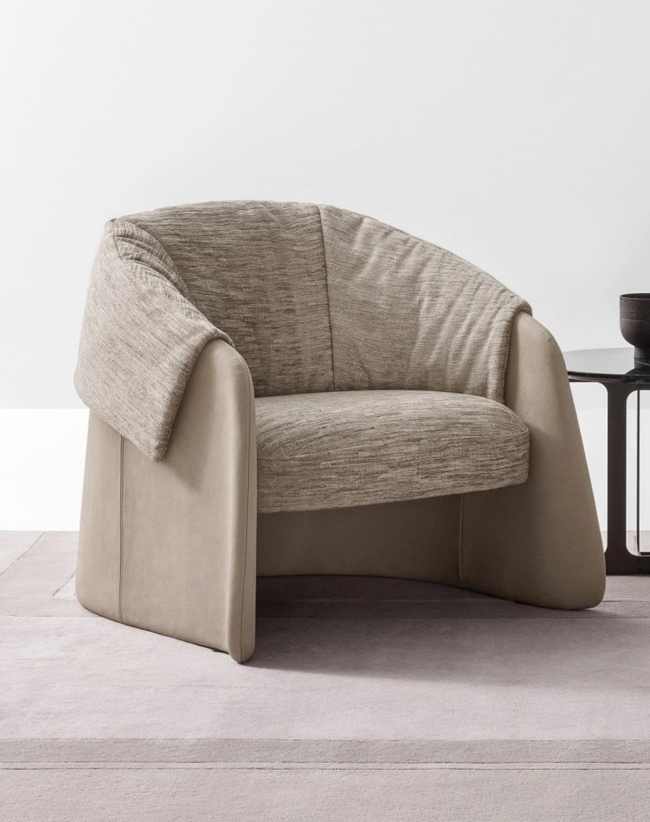 A contemporary lounge chair featuring a two-tone upholstery design, with a smooth, light beige outer shell forming wide, curved armrests and base, and a contrasting textured light brown fabric on the deep seat cushion and draped backrest. The chair has a substantial, low-profile silhouette with soft, rounded lines. — 3D model