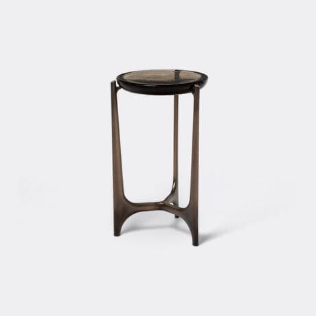 A round-topped side table with a dark, textured surface and a bronze-colored metal base. The base features a unique, stylized design with three curved legs that converge towards the bottom, forming a stable tripartite support. The legs have a smooth, polished finish. The tabletop appears to be made of a dark material, possibly wood or a composite, with a visible textured pattern. — 3D model