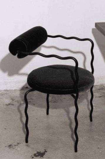 A black armchair with a uniquely designed frame and upholstery. The frame is constructed from thin, wavy metal rods that form the legs, arms, and back support. The seat and a cylindrical headrest are upholstered in a dark, textured fabric. — 3D model