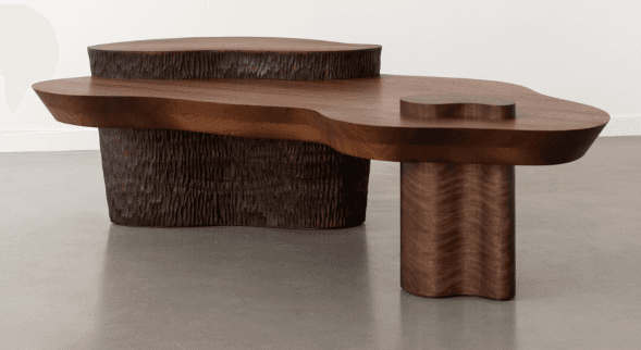 A sculptural, multi-tiered coffee table crafted from dark walnut wood. It features an organic, freeform tabletop with a smaller, raised circular platform on one end, and an integrated, slightly raised heart-shaped detail on the main surface. The table is supported by two distinct bases: a large, textured chiseled base with a roughly cylindrical form, and a smaller, smooth cylindrical leg with a subtle undulating wavy profile. The overall design emphasizes natural forms and contrasting textures. — 3D model