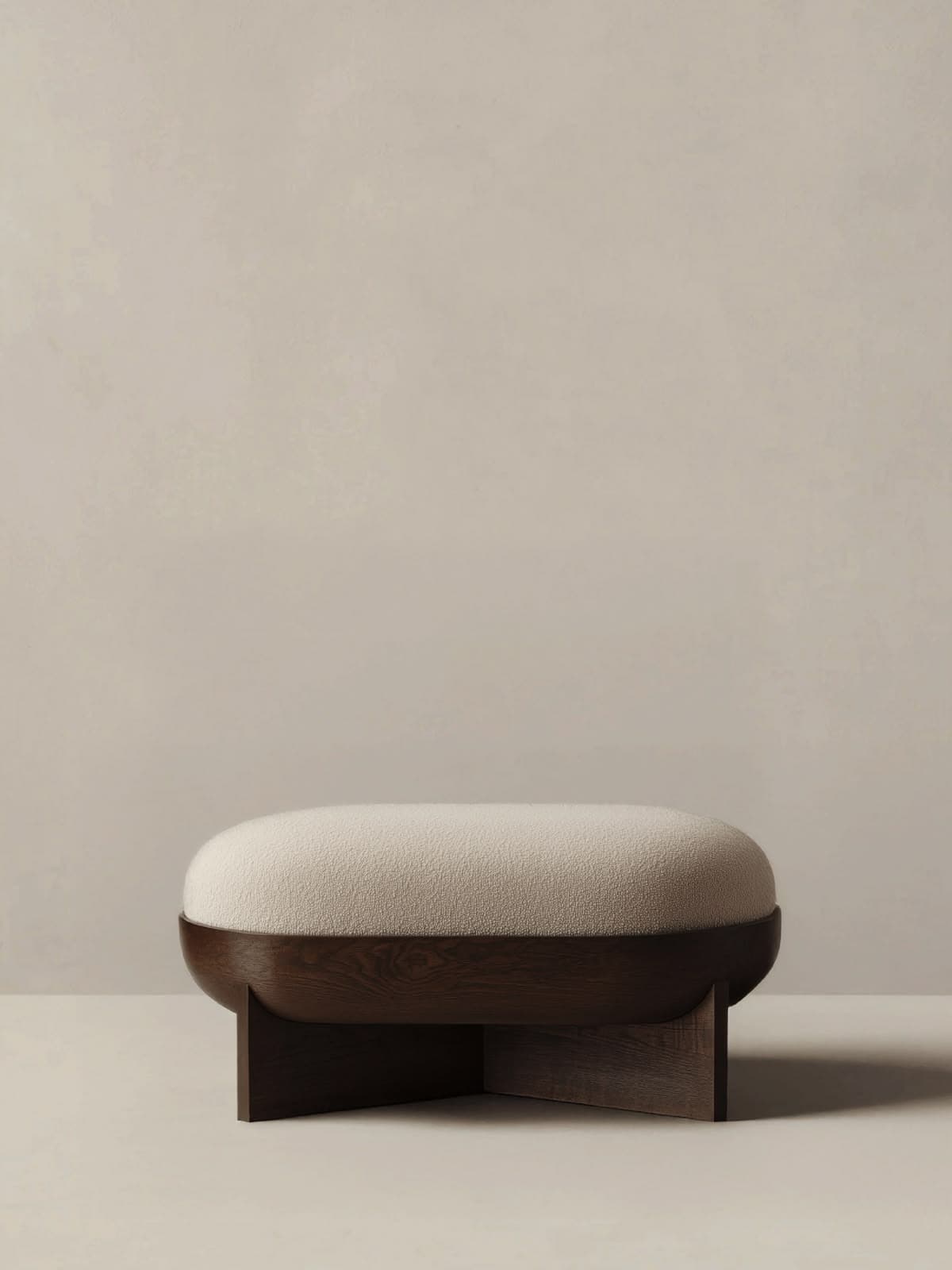 An oval-shaped ottoman with a plush, light-colored boucle upholstered top and a distinctive, dark-stained solid wood base. The base features a sculptural, integrated design that cradles the cushioned top and forms the support structure. The piece has a contemporary, organic modern aesthetic. — 3D model