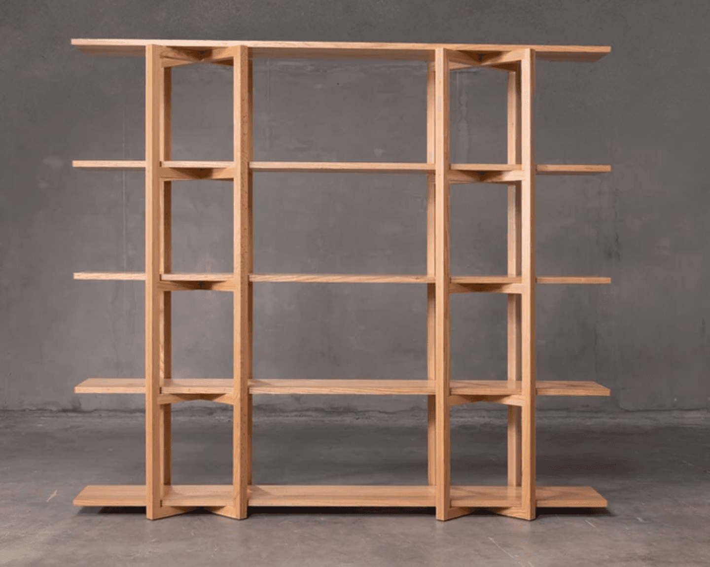 A modern, minimalist bookshelf with five shelves supported by a light wood frame. The shelves are horizontal planes, and the supporting structure consists of vertical elements connected by angled pieces, creating an open, airy design. — 3D model