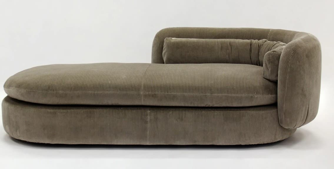 A modern chaise lounge upholstered in taupe corduroy fabric. It features a rounded, low-profile design with thick, plush cushioning. The piece has a single armrest that curves upwards and a bolster pillow. The construction appears substantial and comfortable. — 3D model