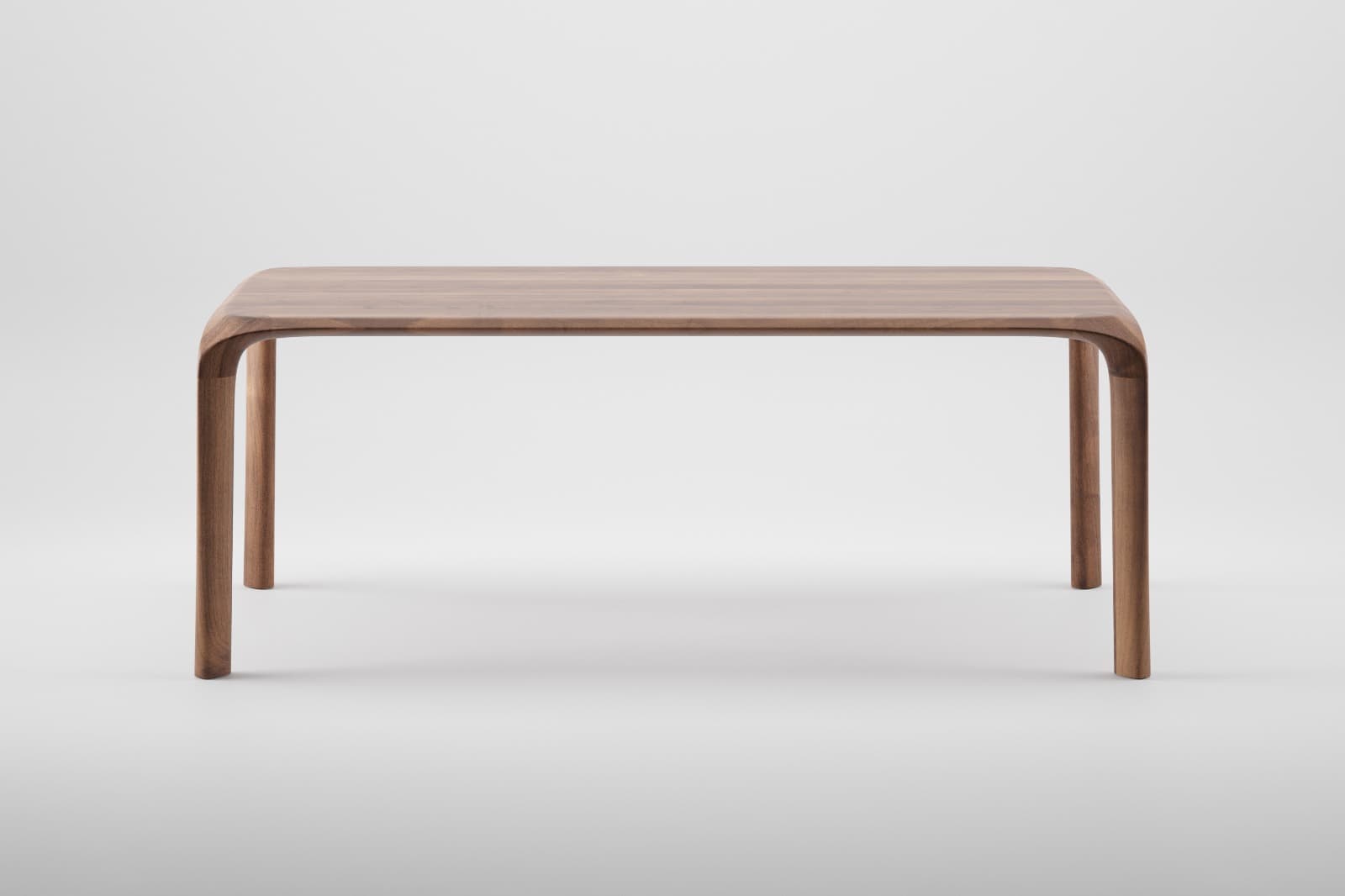 A rectangular solid wood table with smoothly rounded corners and legs that are seamlessly integrated into the tabletop through gentle curves. The table exhibits a minimalist design, crafted from a medium-brown wood, likely walnut, showcasing a fine grain. — 3D model