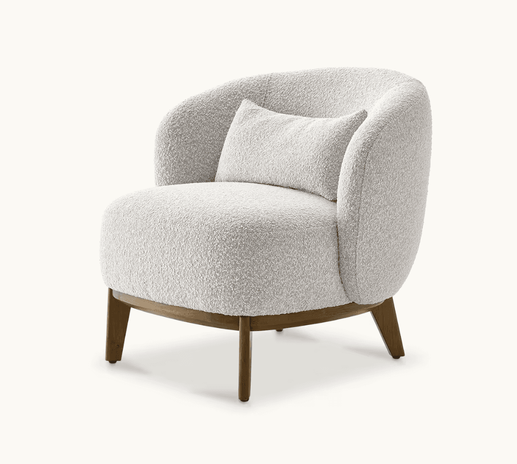 A rounded armchair with a plush, textured upholstery and a matching lumbar pillow. The armchair features a low-profile wooden base and four tapered wooden legs. — 3D model