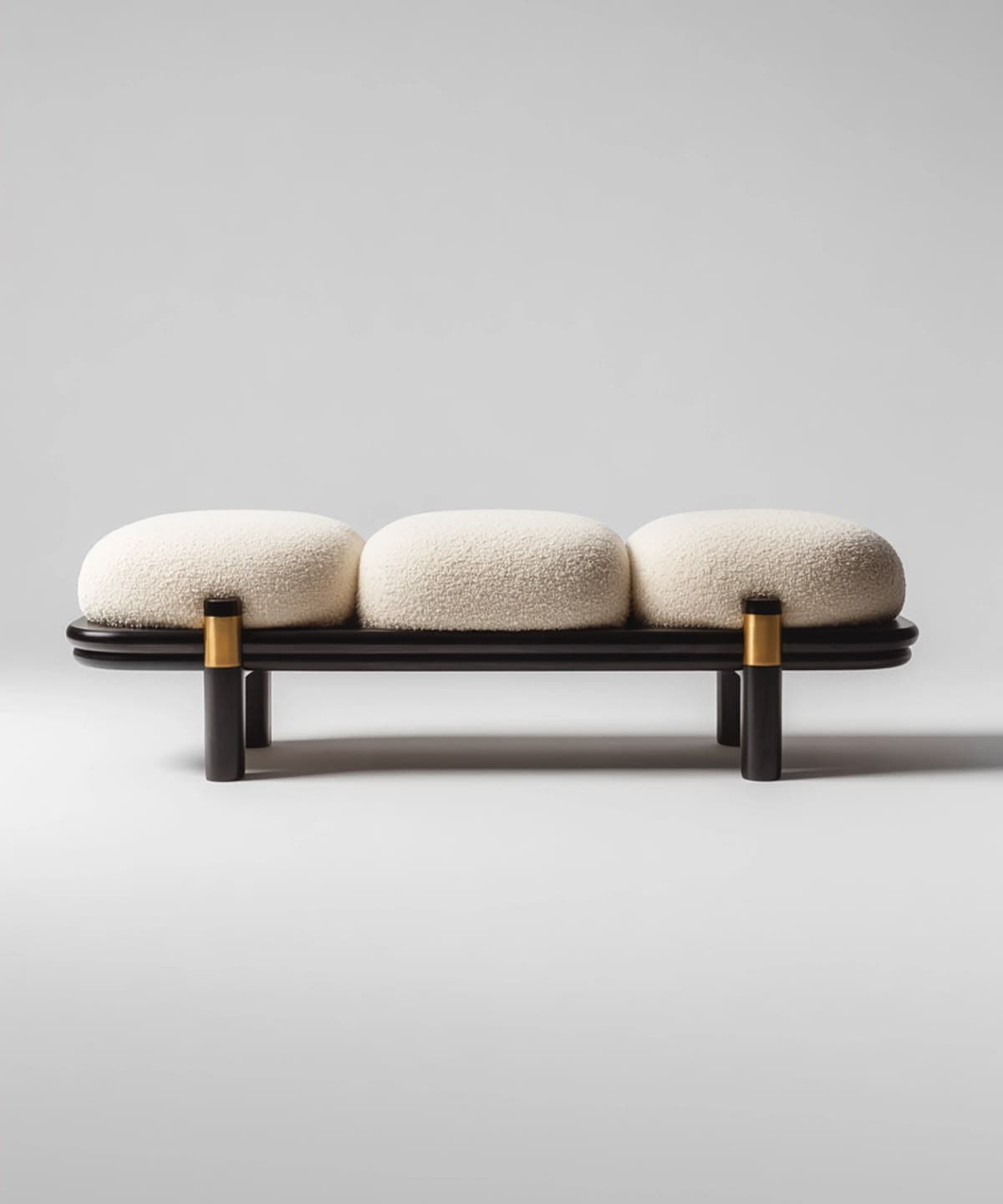 A modern bench featuring three individual, pill-shaped upholstered cushions in off-white bouclé fabric, resting on a dark-stained, subtly curved wooden platform supported by cylindrical dark wood legs with polished brass accents. — 3D model