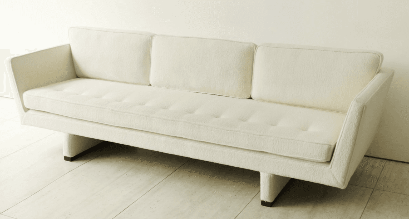 A contemporary three-seater sofa upholstered in an off-white bouclé-like fabric, featuring a single button-tufted seat cushion, three loose back cushions, and integrated wide arms resting on a recessed, block-like base. — 3D model