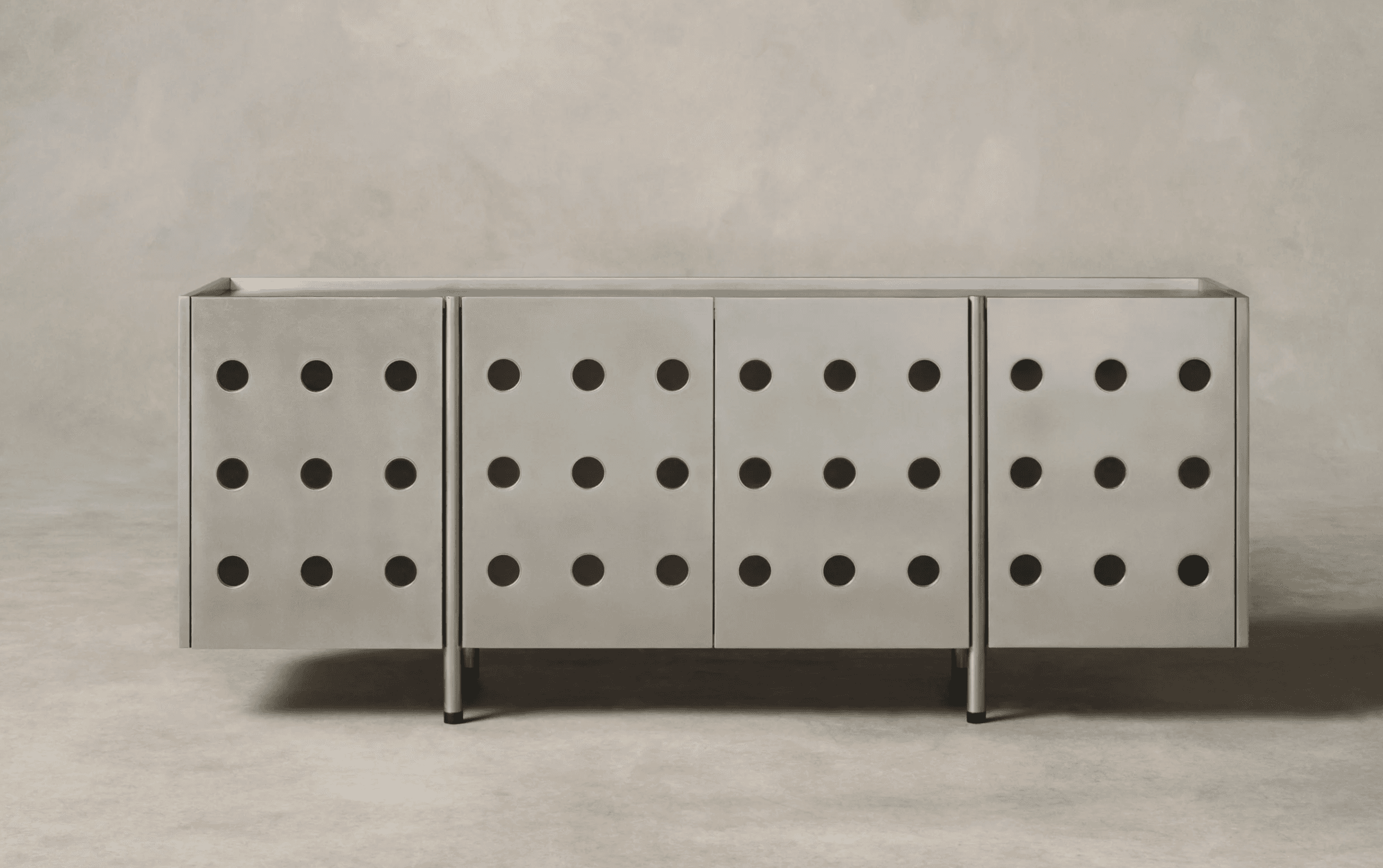 A modern sideboard with a brushed metal finish and a grid of circular perforations on each of its four door panels. The piece is supported by slender, dark cylindrical legs. — 3D model