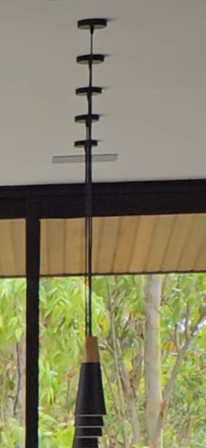 A modern pendant light featuring a series of stacked, progressively smaller black conical shades, capped by a light-colored wood accent. The light is suspended from a black cord, which connects to a ceiling canopy with multiple disc-shaped elements, suggesting a height adjustment mechanism. The overall design is minimalist and contemporary. — 3D model