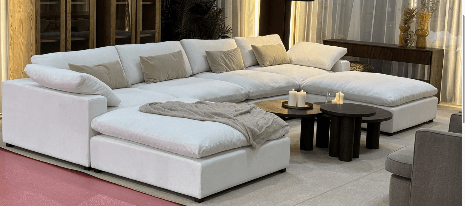 A modular sectional sofa with multiple seating components arranged in a U-shape. It features a low profile, deep seating, and ample cushioning. The sofa is upholstered in a white material and comes with several throw pillows in neutral tones. A beige knitted throw is draped over one of the chaise sections. — 3D model