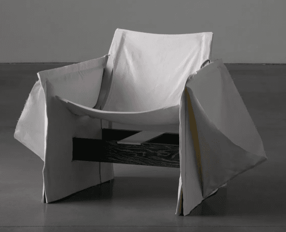 A contemporary lounge chair featuring a dark-stained slatted wooden frame over which a light grey fabric is loosely draped to form the seat, back, and armrests. The design is deconstructed and minimalist. — 3D model