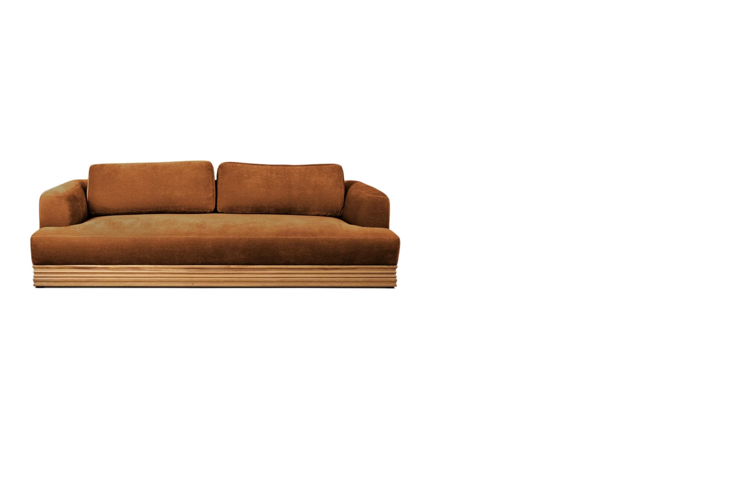 A modern sofa with a plush, upholstered seat and back cushions, and a distinctive slatted wooden base. The upholstery appears to be a velvet or similar fabric in a warm brown or terracotta hue. The sofa has a low profile with substantial armrests that extend to the same height as the back cushions. — 3D model